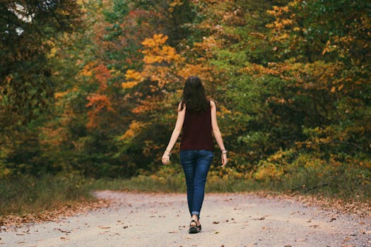 A young woman walks down a colorful autumn forest path, surrounded by vibrant leaves.
